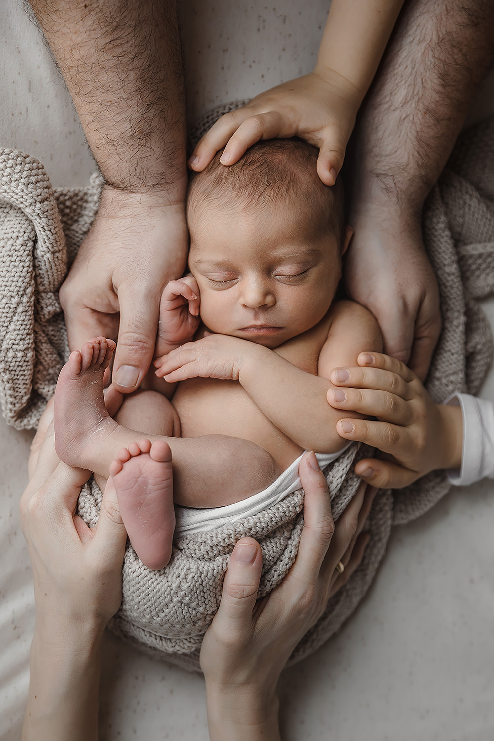 Neugeborenenfoto eines kleinen Mädchens mit den Händen der Eltern und Geschwister
